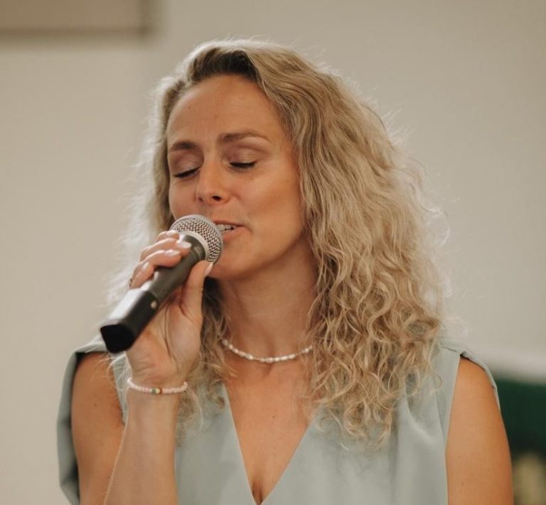 Chantal Will singt mit Mikrofon auf einem Foto unter dem Veranstaltungsplakat der Hochzeitsmesse im Quellenhof Aachen.